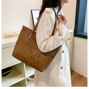 Close-up of a large printed tote bag featuring brown leather straps and letter patterns
