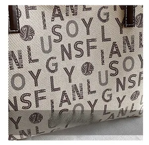 Detailed close-up of beige canvas tote bag featuring brown letter jacquard and leather handle