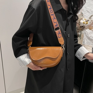 Brown semi-circle saddle bag with wavy flap and vintage patterned wide strap on black coat