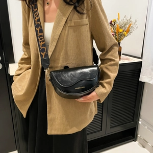 Minimalist black saddle bag with glossy texture and wide strap shown on a model