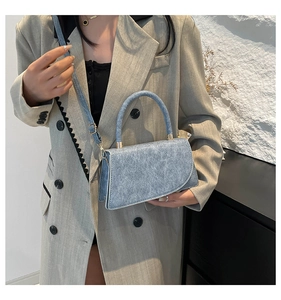 Detail view of light blue textured handbag with unique asymmetrical flap and gold hardware