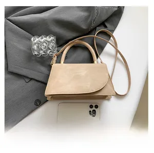 Detail view of beige crossbody bag with curved flap and smartphone for size reference