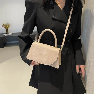 Elegant beige matte textured handbag with gold hardware on black coat background