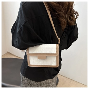 Detail of white crocodile texture leather crossbody bag with brown trim on model