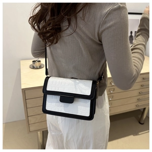 Detail of white crocodile embossed texture and black leather stitching on a crossbody bag