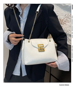Detailed view of white leather shoulder bag with gold chain and geometric lock on a model