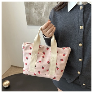 Detail of pink corduroy tote bag with red strawberry print held by model indoors