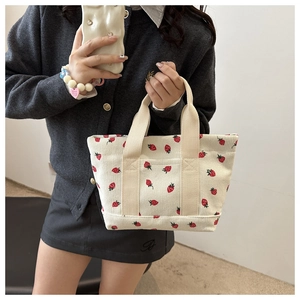 Detailed close-up of a white corduroy tote bag with cute red strawberry print and handle