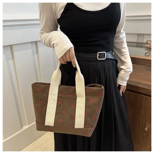 Detail of brown corduroy tote bag featuring red strawberry prints and wide fabric handles