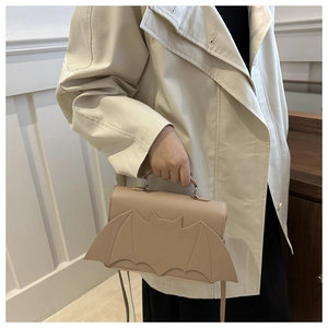 Gros plan du sac à bandoulière beige en forme de chauve-souris porté avec un trench