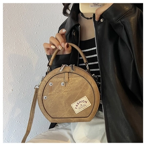 Détail d'un sac rond marron en patchwork de denim porté avec une veste en cuir noir