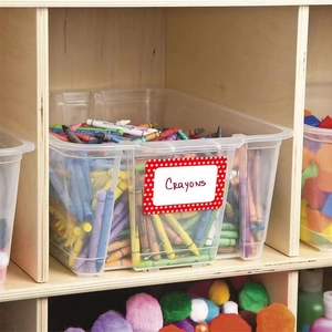 Clear plastic storage bin with red star label holding colorful crayons on wood shelf