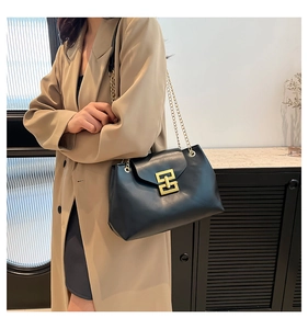 Close-up of black leather tote bag with gold chain strap and geometric metal buckle lock