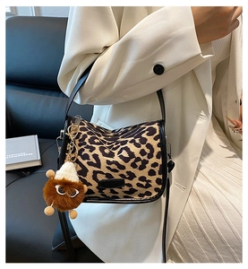Detail of leopard print shoulder bag with black leather strap and brown plush monster charm