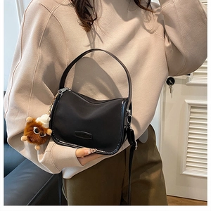 Detail of black nylon pillow bag with round handles and plush doll pendant on model