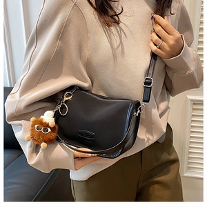 Detail of black faux leather crescent shoulder bag with a cute brown plush charm