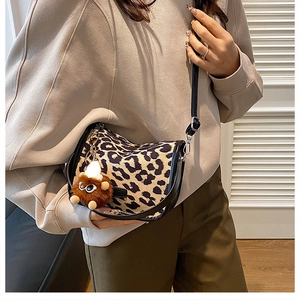 Detail of leopard print crossbody bag featuring a plush brown monster charm and leather strap