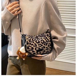 Detail of leopard print crossbody saddle bag featuring a black strap and plush charm