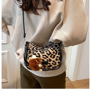 Leopard print crossbody saddle bag with black trim and brown pompom on olive pants