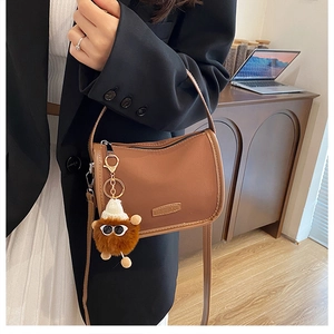 Close-up of brown matte PU leather handbag featuring a gold FASHION metal plate and plush charm