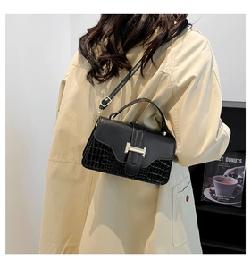 Detail of black crossbody bag with gold H-clasp and crocodile texture on beige trench coat