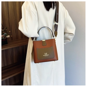 Detail of a brown and olive leather bucket bag worn with a stylish white long coat