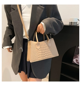 Detail of beige crocodile embossed handbag with gold hardware and stylish top handle