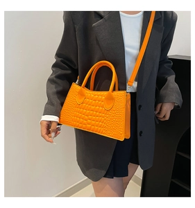 Detail of bright orange crocodile pattern handbag worn with casual grey blazer