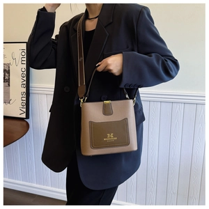 Fashionable brown bucket bag with wide jacquard strap worn by a model in a black suit