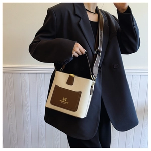 Detail of contrast color leather bucket bag with wide strap on a model in black suit