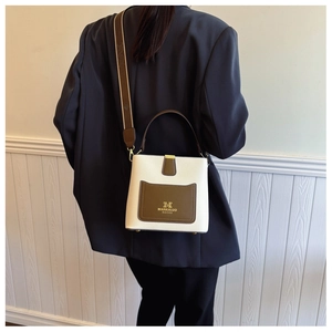 Detail of a minimalist bucket bag showing wide strap and leather contrast on model