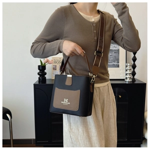 Detail of black and brown leather bucket bag with wide strap and golden hardware