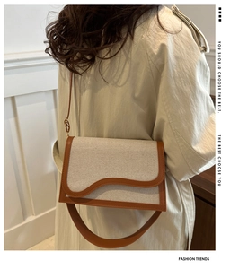Detail of canvas crossbody bag featuring brown leather trim and wavy edge flap design