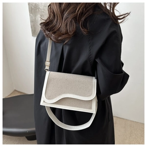 Detail view of canvas shoulder bag with white leather trim and wavy flap design on model