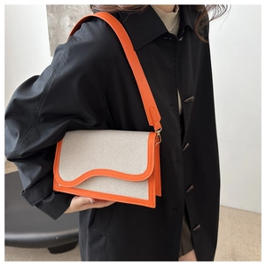 Detail of a color-blocked canvas shoulder bag with orange leather trim and wave-edge flap