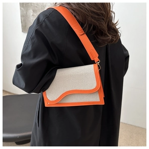 Detail of grey canvas crossbody bag with orange leather trim on a model in a black coat