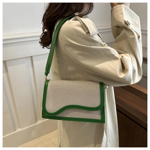 Detail of beige canvas and green leather crossbody bag worn with a chic trench coat