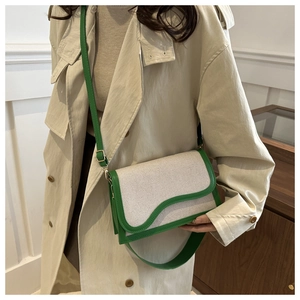 Detail of canvas shoulder bag with green leather trim and adjustable strap on a beige coat