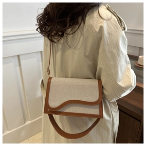 Detail of canvas shoulder bag with wave edge flap and contrast leather trim on a model