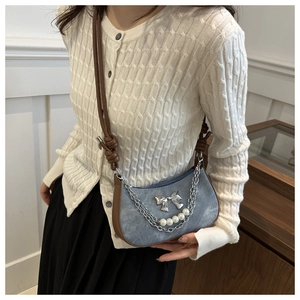 Close-up of light blue denim crossbody bag with white pearls and silver bow detail