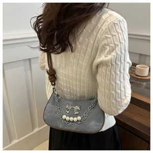 Detail of washed denim shoulder bag featuring silver bow, pearl chain and knot strap