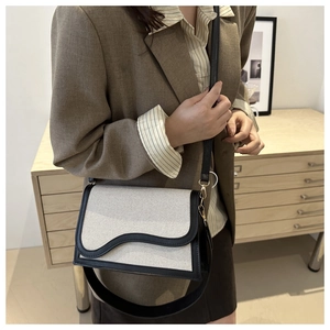 Detail of a chic shoulder bag featuring cream canvas with black leather wavy flap design