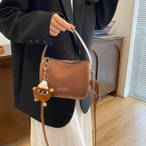 Brown matte leopard pillow bag with plush monster charm held by a model in a cozy setting