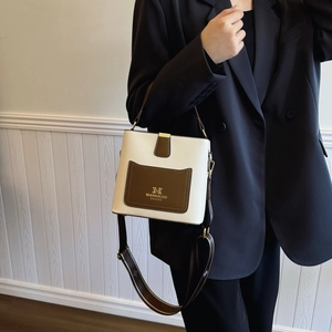 Minimalist cream and brown bucket bag with wide strap shown on model's shoulder