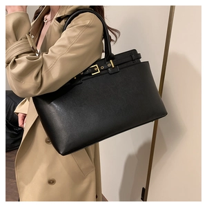 Detail of a large black tote bag with gold buckle on a khaki trench coat shoulder