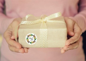 Close-up of floral Thank You sticker on a brown paper gift box held by female hands