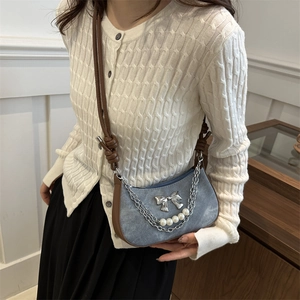 Blue denim crossbody bag with pearl strap and silver bow detail shown on a model
