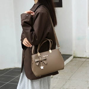 Khaki brown tote bag with bow detail and star pendant, shown in a street style setting