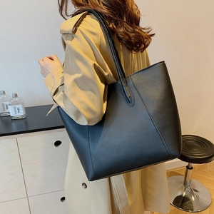 Große schwarze minimalistische Tote Bag aus mattem Leder getragen mit einem Trenchcoat