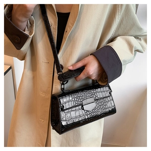 Detail of black crocodile texture handbag with glossy finish and metal clasp on trench coat